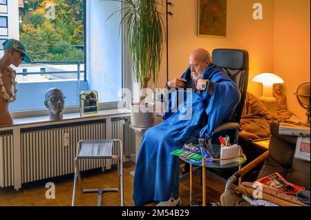 Vecchio avvolto in coperte, risparmiare energia, congelare a causa di Putin, risparmiare costi di riscaldamento, bassa temperatura ambiente, Baviera, Germania Foto Stock