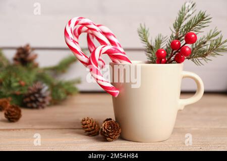 Tazza di gustose canne di caramelle, rametto di abete e coni su tavola di legno Foto Stock