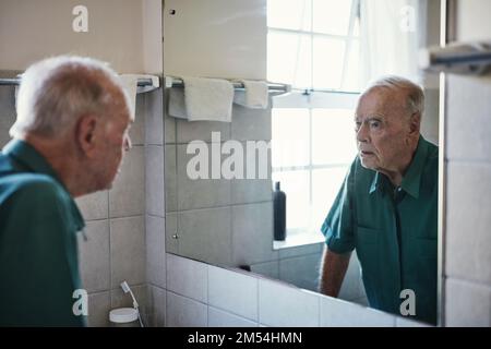 Come ho fatto a diventare così vecchio. un uomo anziano che guarda nello specchio del suo bagno. Foto Stock