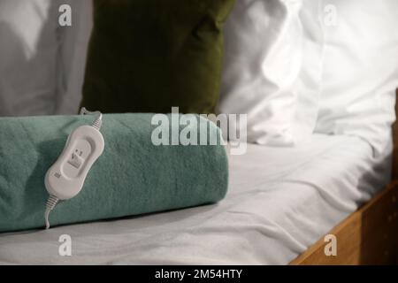 Imbottitura riscaldante elettrica ripiegata con controller sul letto di notte, primo piano Foto Stock