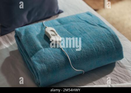 Imbottitura riscaldante elettrica ripiegata con controller sul letto di notte, primo piano Foto Stock