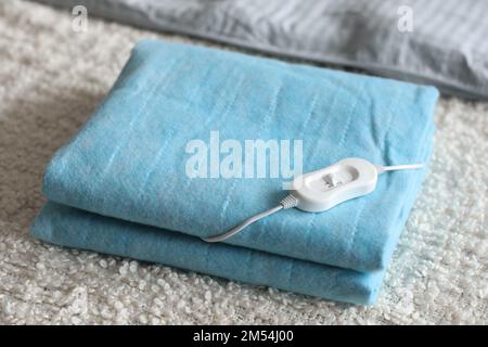 Cuscino riscaldante elettrico ripiegato con controller su coperta bianca in camera da letto, primo piano Foto Stock