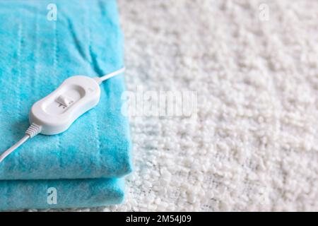 Cuscino riscaldante elettrico ripiegato con controller su coperta bianca in camera da letto, primo piano Foto Stock