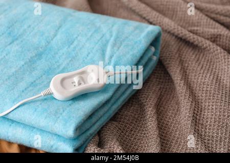 Cuscino riscaldante elettrico ripiegato con controller su coperta in camera da letto, primo piano Foto Stock