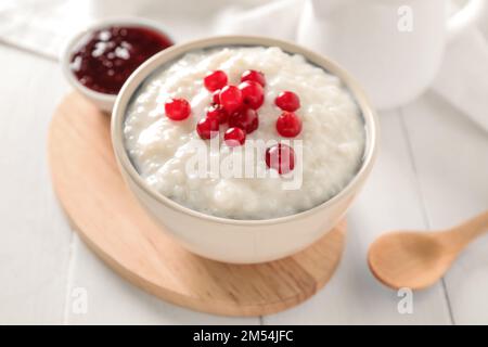 Ciotola con delizioso budino di riso, mirtillo rosso e marmellata su un tavolo di legno bianco Foto Stock