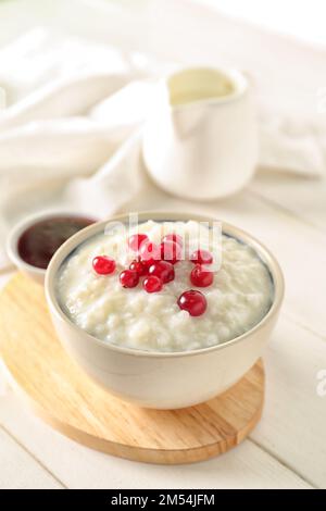 Ciotola con delizioso budino di riso, mirtillo rosso e marmellata su un tavolo di legno bianco Foto Stock