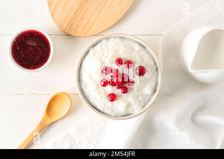 Ciotola con delizioso budino di riso, mirtillo rosso e marmellata su un tavolo di legno bianco Foto Stock