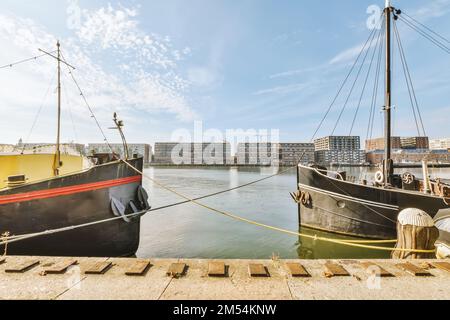 due barche ormeggiate al molo di fronte a un grande edificio e cielo blu con alcune nuvole bianche sopra di loro Foto Stock