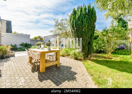 un'area cortile con un tavolo e sedie al centro, circondata da alberi verdi su entrambi i lati del cortile Foto Stock