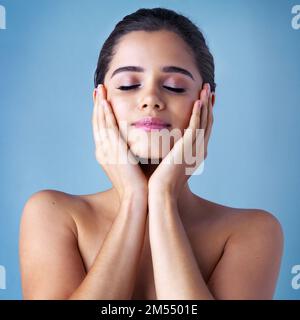 Si innamorerà del suo nuovo regime di cura della pelle. Studio di una bella giovane donna che posa su uno sfondo blu. Foto Stock