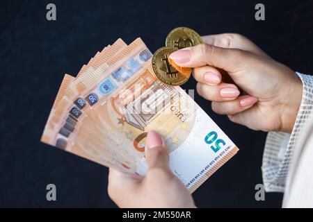 Mani di closeup donna che tengono monete d'oro di cripto e banconote in euro, indossando una giacca bianca. Foto Stock
