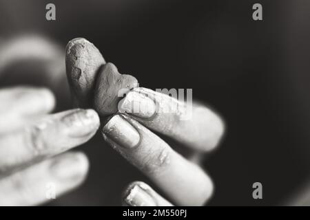 Cuore fatto di argilla di vasaio nelle mani di un maestro vasaio. Concetto di amore. Bianco e nero. Foto Stock