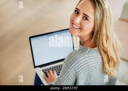 Trascorrere un po 'di tempo sul mio blog. Ritratto ad angolo alto di una giovane donna attraente che utilizza il suo notebook a casa. Foto Stock