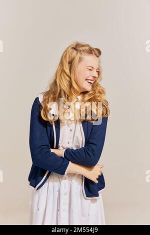 Ritratto di bella giovane donna bionda alla moda con capelli retrò vestito vintage ridendo isolato su sfondo grigio. Emozioni Foto Stock