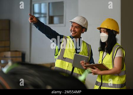 Responsabili e addetti al magazzino che controllano l'inventario in un magazzino con scatole imballate sugli scaffali Foto Stock