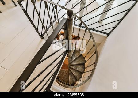 una scala a chiocciola in una casa moderna, presa dall'alto verso il pavimento sotto le sue ringhiere bianche e nere Foto Stock