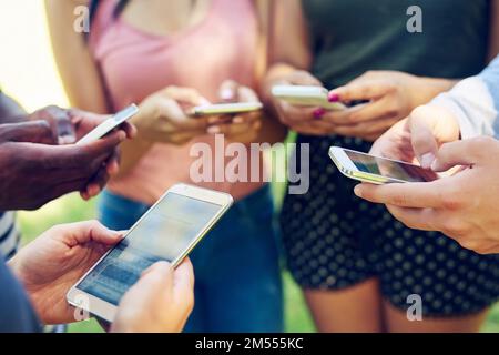 L'età dell'app. un gruppo di amici che usano il telefono insieme all'aperto. Foto Stock