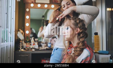 L'artista ragazza trucco fa una treccia per il modello. Foto Stock