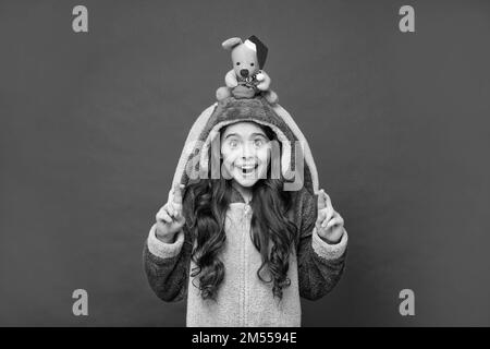 sorprendo il capretto nel pajama comodo tiene il giocattolo di natale su sfondo rosso, homewear Foto Stock