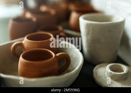 Un primo piano di varie stoviglie di argilla che asciugano su uno scaffale. Un concetto di studio di ceramica. Piatti artigianali, ciotole, pentole, tazze di diversi colori. Vista accogliente. Foto Stock