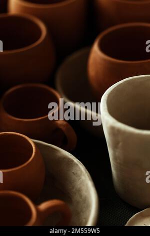 Un primo piano di varie stoviglie di argilla che asciugano su uno scaffale. Un concetto di studio di ceramica. Piatti artigianali, ciotole, pentole, tazze di diversi colori. Vista accogliente. Foto Stock