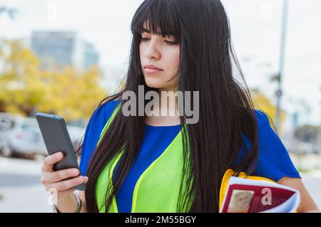 Giovane donna latina caucasica che lavora, ingegnere, nel suo tempo libero controllare le notifiche al telefono, durante la pausa pranzo. Foto Stock