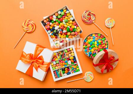 Set di caramelle dolci diverse in una scatola di carta con un nastro di raso su uno sfondo colorato. Concetto di vacanza. Foto Stock