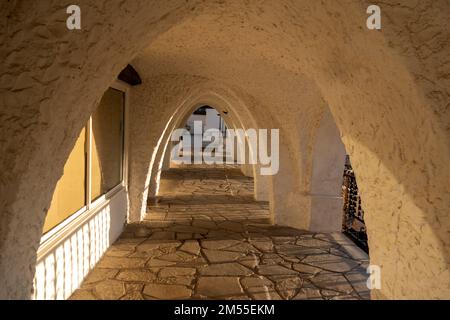 Arco illuminato dal sole con pavimento pavimentato e pareti in gesso la mattina presto fuori dall'edificio dell'hotel sul resort Foto Stock