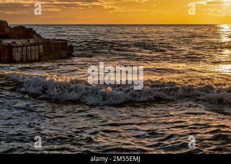 Onde schiumose di mare schiumoso che spruzzi vicino alla banchina al tramonto in estate sul resort Foto Stock