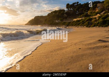 Livello del terreno di onde di mare schiumose che spruzzano sulla spiaggia sabbiosa contro la collina verde e il cielo nuvoloso dell'alba Foto Stock