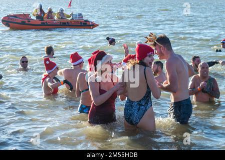 Jubilee Beach, Marine Parade, Southend on Sea, Essex, Regno Unito. 26th Dec, 2022. Come è diventata una tradizione nelle località balneari, un 'Boxing Day DIP' ha avuto luogo nel freddo e ruvido estuario del Tamigi a Southend on Sea, vicino al molo della città, raccogliendo fondi per la Royal National Lifeboat Institution locale. Circa 400 persone sono scesi in acqua, che era di circa 6 gradi Celsius. Molti dei nuotatori coraggiosi indossavano un abbigliamento festivo. La scialuppa di salvataggio RNLI era a portata di mano per motivi di sicurezza. Gruppo di persone in acqua Foto Stock