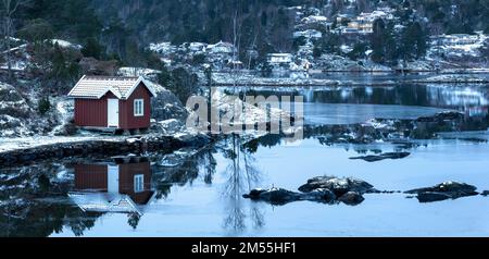 Inverno al mare con piccoli cottage in legno, rocce, boschi nell'ora blu, giorno coperto Foto Stock