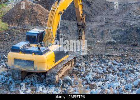 L'escavatore giallo con un martello sul braccio distrugge i resti di un edificio su un mucchio di rifiuti Foto Stock