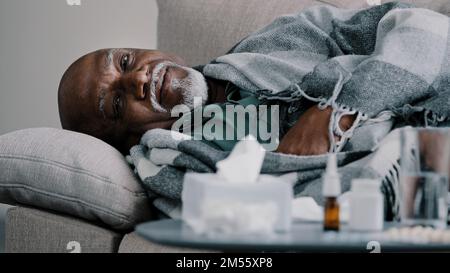 Vecchio calvo sopportato sovrappeso uomo di mezza età nonno africano malato uomo d'affari sdraiato sul divano a casa con febbre ad alta temperatura, malattia fredda Foto Stock