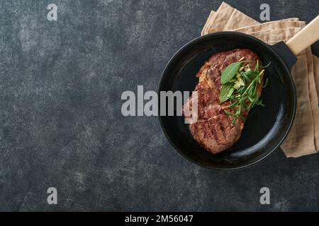 Bistecche. Bistecca di carne alla griglia a fette New York o Ribeye con spezie rosmarino e pepe in teglia di ferro nera su tavola di marmo su vecchio sfondo di legno. Parte superiore v Foto Stock