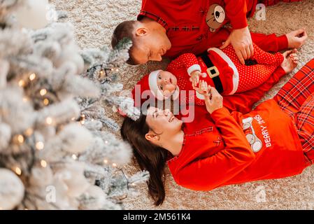 Natale famiglia baciare e abbracciare. Il bambino ha sorpreso sua madre e suo padre con un regalo di Natale. Famiglia vicino all'albero di natale. Buon Natale e. Foto Stock