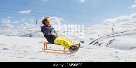 Ragazzo che scivola su una slitta di legno in una stazione sciistica Foto Stock