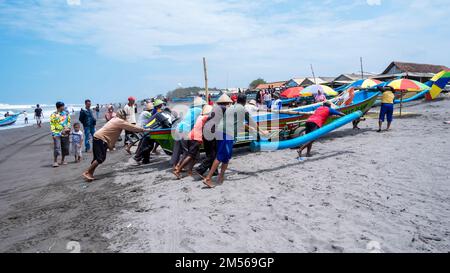 Yogyakarta, Indonesia - 27 marzo 2022: Dopo il ritorno dalla pesca in mare, i pescatori spingono le barche sulla terraferma Foto Stock