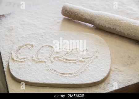 La parola accogliente scritta in farina sul tavolo da cucina Foto Stock