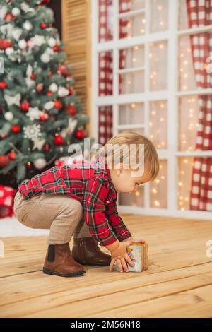 bambino in pantaloni e una camicia a quadri gioca sul pavimento con cubo di legno Foto Stock