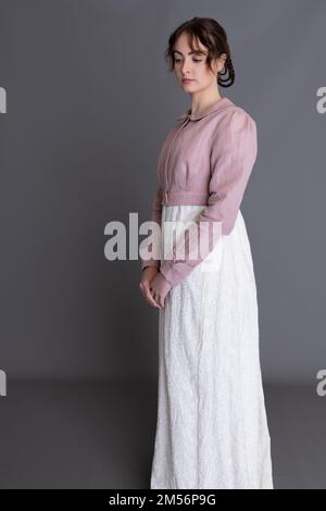 Una donna del periodo Regency che indossa un abito ricamato in crema con spencer in lino rosa sullo sfondo di un semplice studio Foto Stock