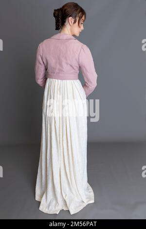 Una donna del periodo Regency che indossa un abito ricamato in crema con spencer in lino rosa sullo sfondo di un semplice studio Foto Stock