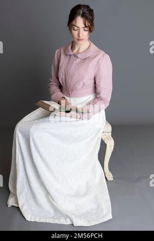 Una donna del periodo Regency che indossa un abito ricamato in crema con spencer in lino rosa sullo sfondo di un semplice studio Foto Stock