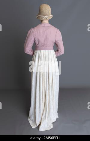 Una donna del periodo Regency che indossa un abito ricamato in crema con spencer in lino rosa sullo sfondo di un semplice studio Foto Stock