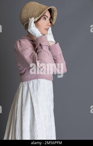 Una donna del periodo Regency che indossa un abito ricamato in crema con spencer in lino rosa sullo sfondo di un semplice studio Foto Stock