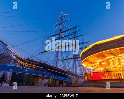 Londra, Greenwich, Inghilterra - 26 dicembre 2022: Scena natalizia con una giostra in movimento davanti alla nave Cutty Sark nella penisola di Greenwich Foto Stock