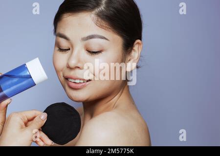 giovane donna asiatica con pulitore per il trucco e tampone di cotone nero su sfondo blu. Foto Stock