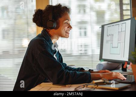 Sorridente Afro american donna interior designer in cuffie lavora in casa ufficio Foto Stock