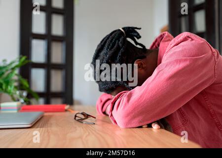 Uomo afroamericano stanco addormentato che prende il pisolino con la testa appoggiata sul desktop con il laptop in ufficio Foto Stock