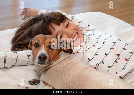 Una ragazza di 10 anni e il suo cane animale domestico che posa accogliente sul letto Foto Stock